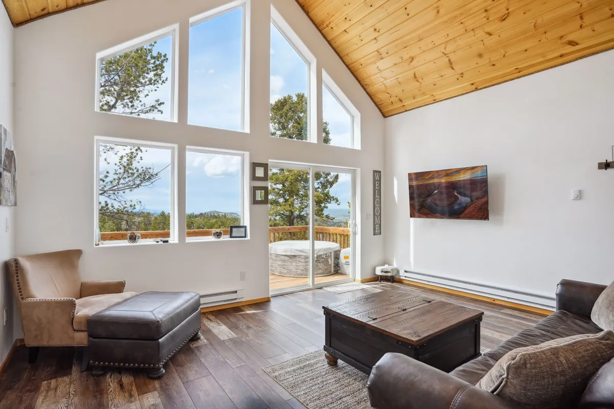 A cozy seating area with plush chairs and a coffee table set beneath a wooden ceiling. Massive windows dominate one wall, providing unobstructed views of the surrounding mountains and letting in generous amounts of daylight.