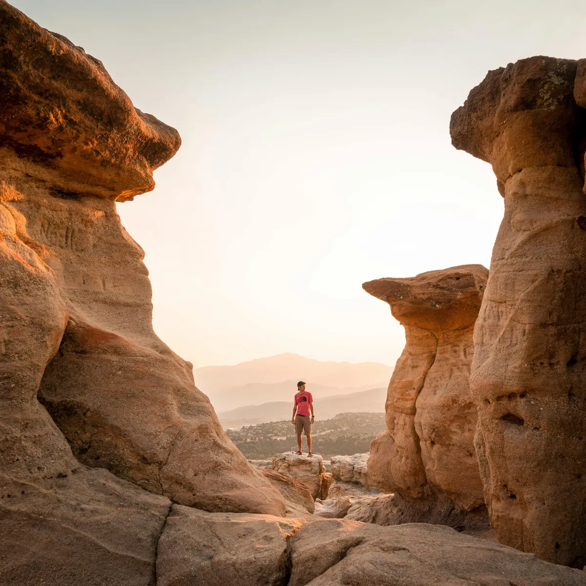 A dramatic landscape featuring rugged rock formations in the foreground, a lone individual standing contemplatively on the rocks, and a distant view of mountains under a striking sky. The scene captures the spirit of exploration, offering a sense of solitude, reflection, and the breathtaking beauty of the area.