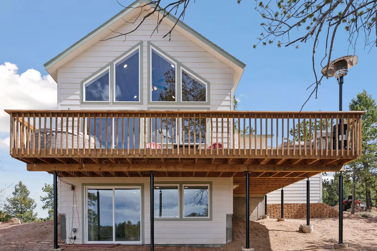 A wide-angle view of a large front deck with striking triangular windows and a wooden railing, offering sweeping views of the mountains and sky. The inviting setting is ideal for sunset watching or stargazing.