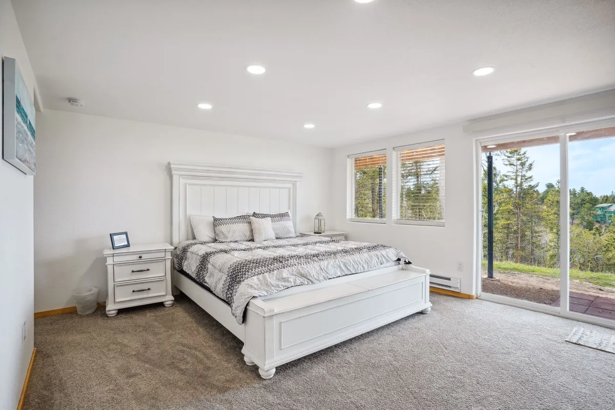 A tranquil bedroom scene with a simple, comfortable bed positioned near windows and a nightstand. The view outside the windows hints at the scenic surroundings, and the setup is ideal for enjoying peaceful evenings or morning light.