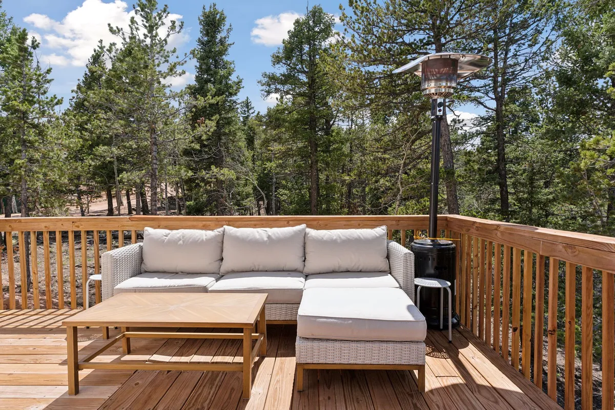 An outdoor entertaining space with a chic sectional sofa, wooden coffee table, and patio heater, all surrounded by tall trees. The setting exudes tranquility, perfect for both lively gatherings and peaceful moments in nature.