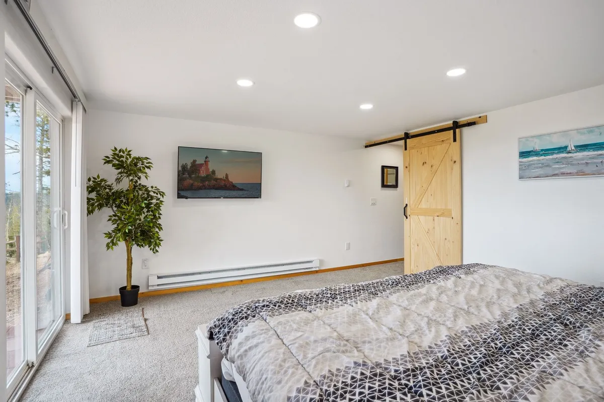 A bright and inviting bedroom featuring a large bed, a sliding glass door that opens to potential mountain views, a potted plant, and cozy decor. The abundance of natural light and the view from the bed capture the idea of waking up in a serene mountain setting, echoing morning coffee moments described in the section.