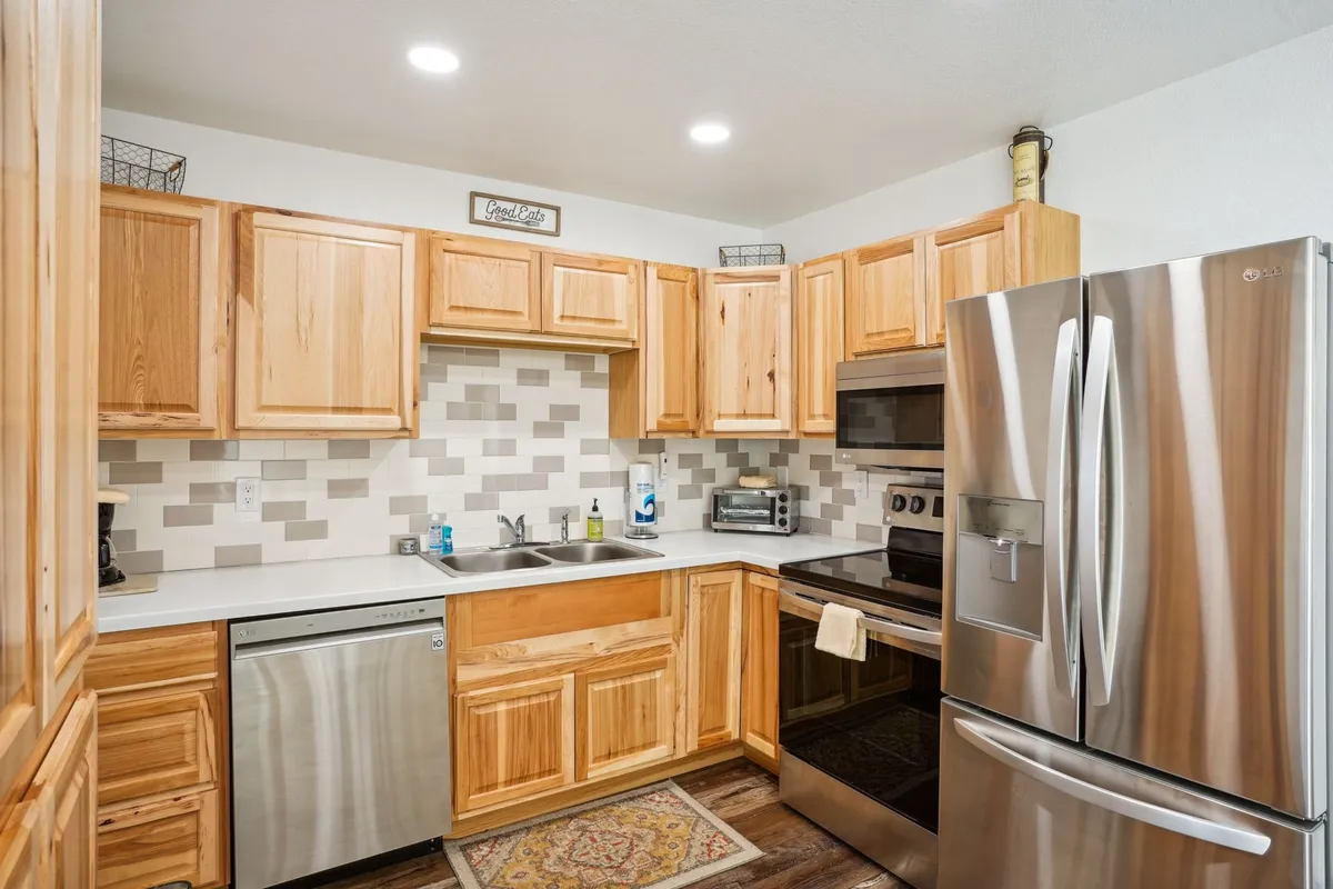 A warm, welcoming kitchen featuring wooden cabinets, stainless steel appliances, a decorative backsplash, and a cozy kitchen rug. The space exudes modern functionality and comfort, with enough room for meal prep and family gatherings.