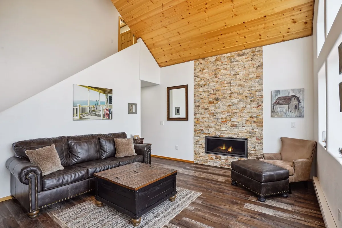 A warmly furnished living room with a leather sofa, stone fireplace, wooden coffee table, and large windows. The scene exudes coziness and comfort, providing a glimpse of spaces perfect for romantic evenings by the fire and relaxation after a day spent exploring nature.
