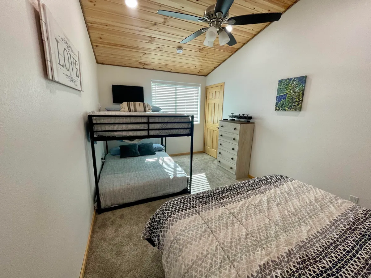 A welcoming family bedroom featuring a bunk bed and a double bed, with a dresser and cheerful artwork on the wall. The setup is both practical and cozy, perfect for families sharing bedtime stories or unwinding together after a day of adventure.