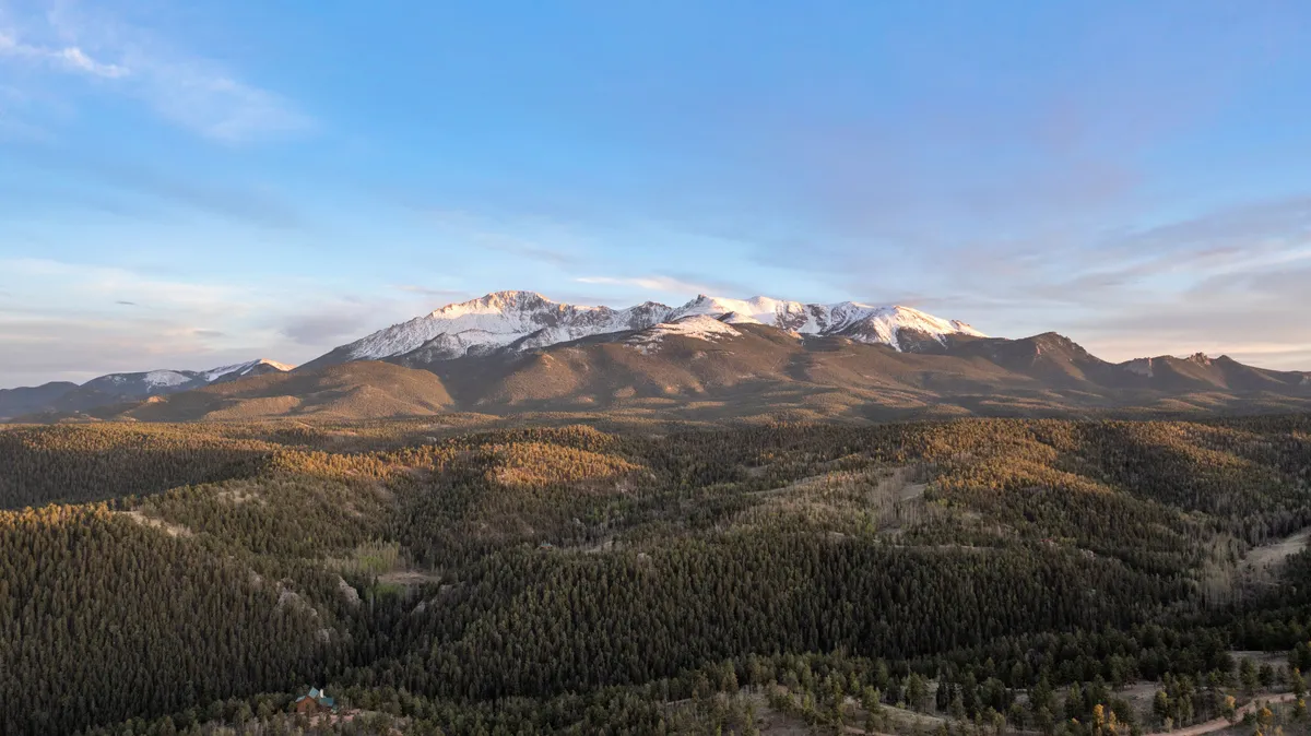 A serene, expansive view of snow-capped mountains and dense forests under a tranquil sky. The vast landscape invites exploration and highlights the natural beauty unique to the Woodland Park area, hinting at opportunities for hiking, photography, and stargazing.